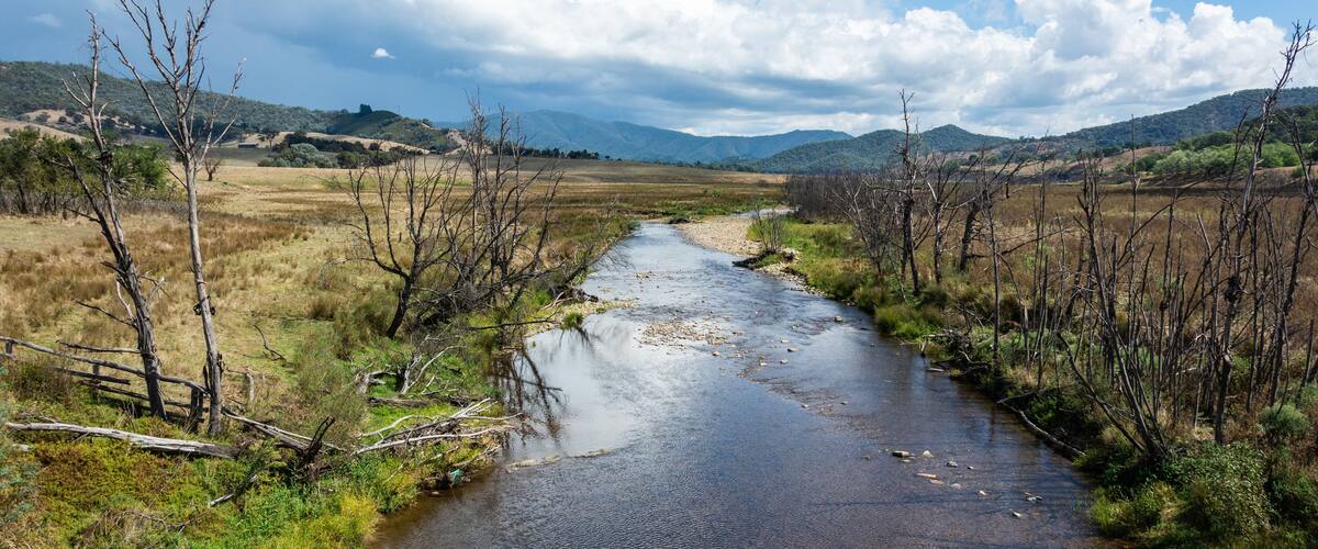 A river flowing through a rural landscape with hills in the background.