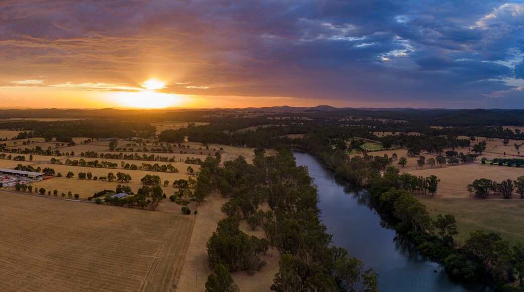 Aerial panorama view of colourful dramatic sunset over farmland alongside an inland river