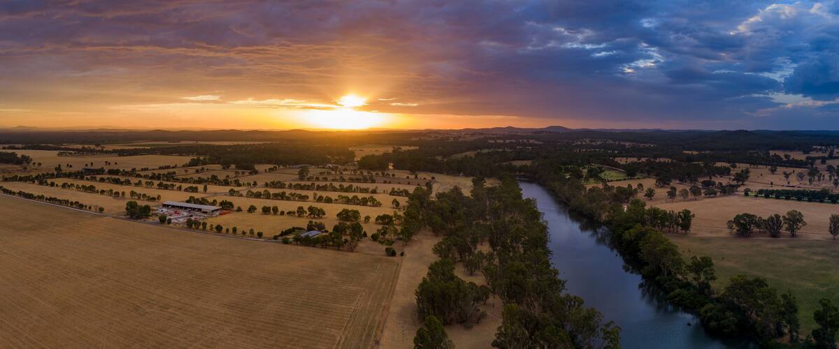Aerial panorama view of colourful dramatic sunset over farmland alongside an inland river