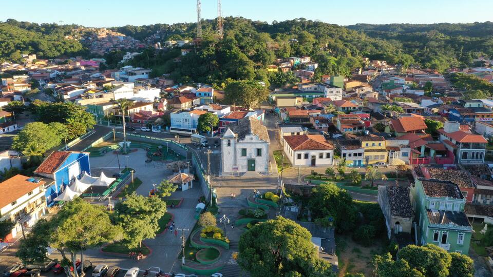 An aerial view of a town with a central plaza, surrounded by colorful buildings and lush greenery.