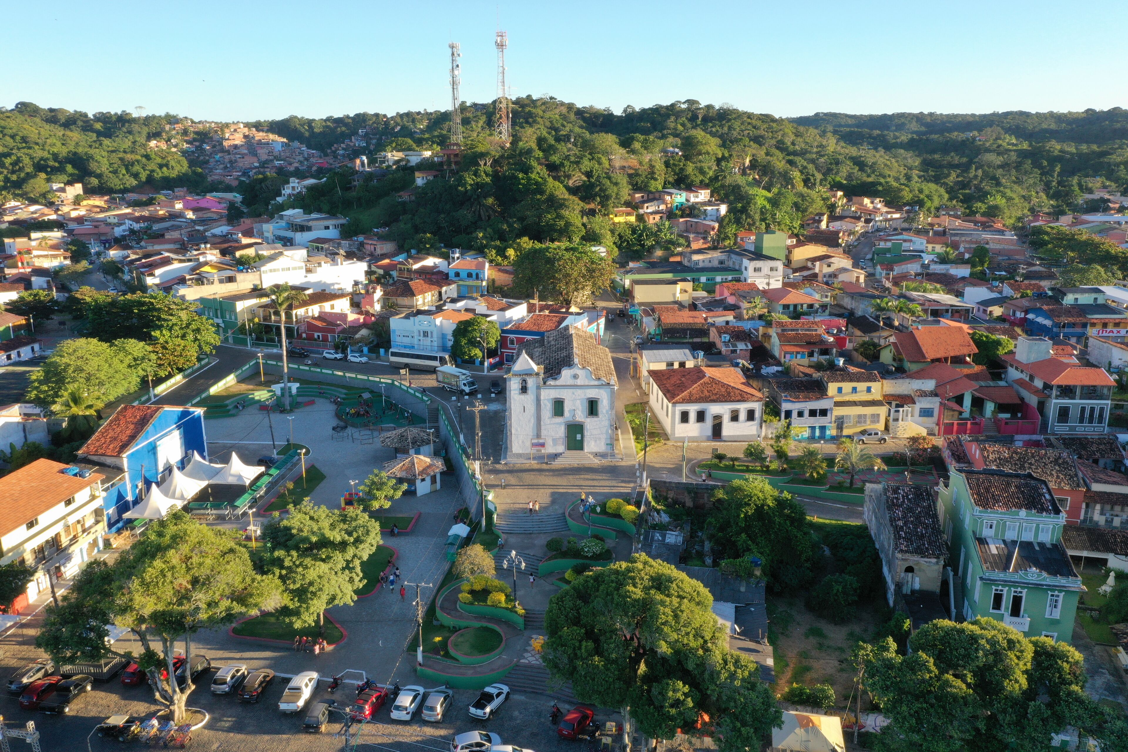 An aerial view of a town with a central plaza, surrounded by colorful buildings and lush greenery.