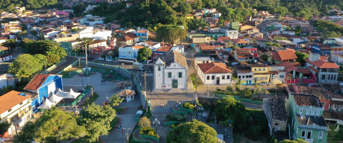 An aerial view of a town with a central plaza, surrounded by colorful buildings and lush greenery.