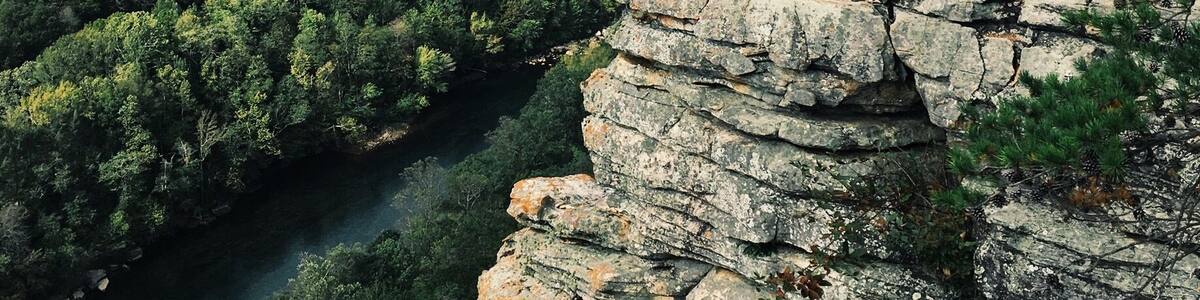 A person sitting on a rocky outcrop overlooking a river and forested valley.