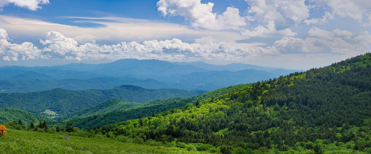 A mountainous landscape with dense forests and rolling hills under a partly cloudy sky.