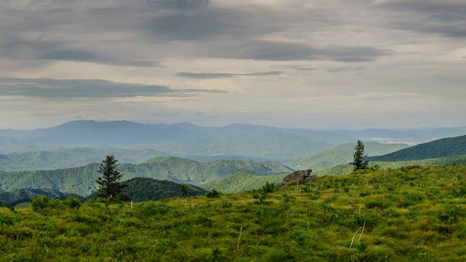 A mountainous landscape with rolling hills, dense greenery, and a cloudy sky.