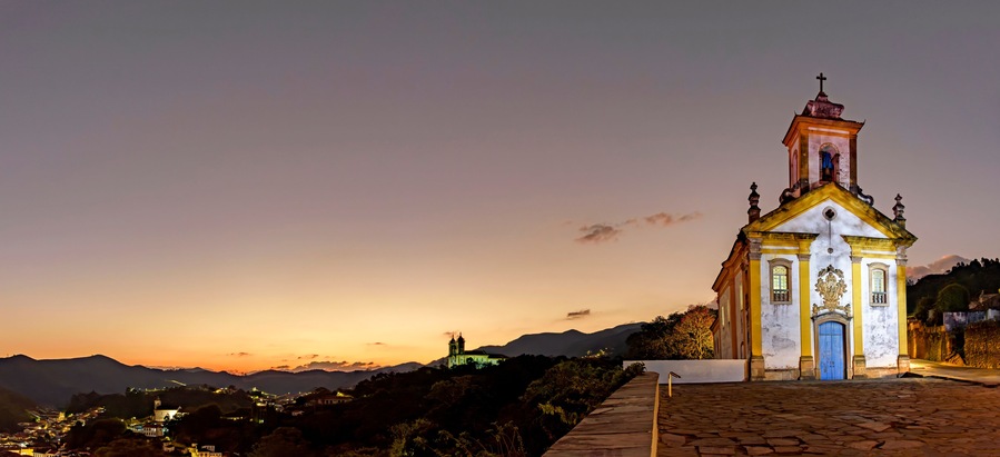 Panoramic image with the baroque style churches and the city illuminated on top of the hill in Ouro Preto, Minas Gerais illuminated during dusk