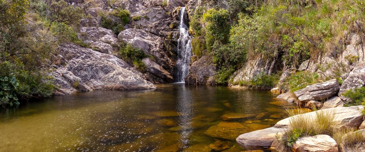 A waterfall cascading into a clear pool surrounded by rocky terrain and greenery.