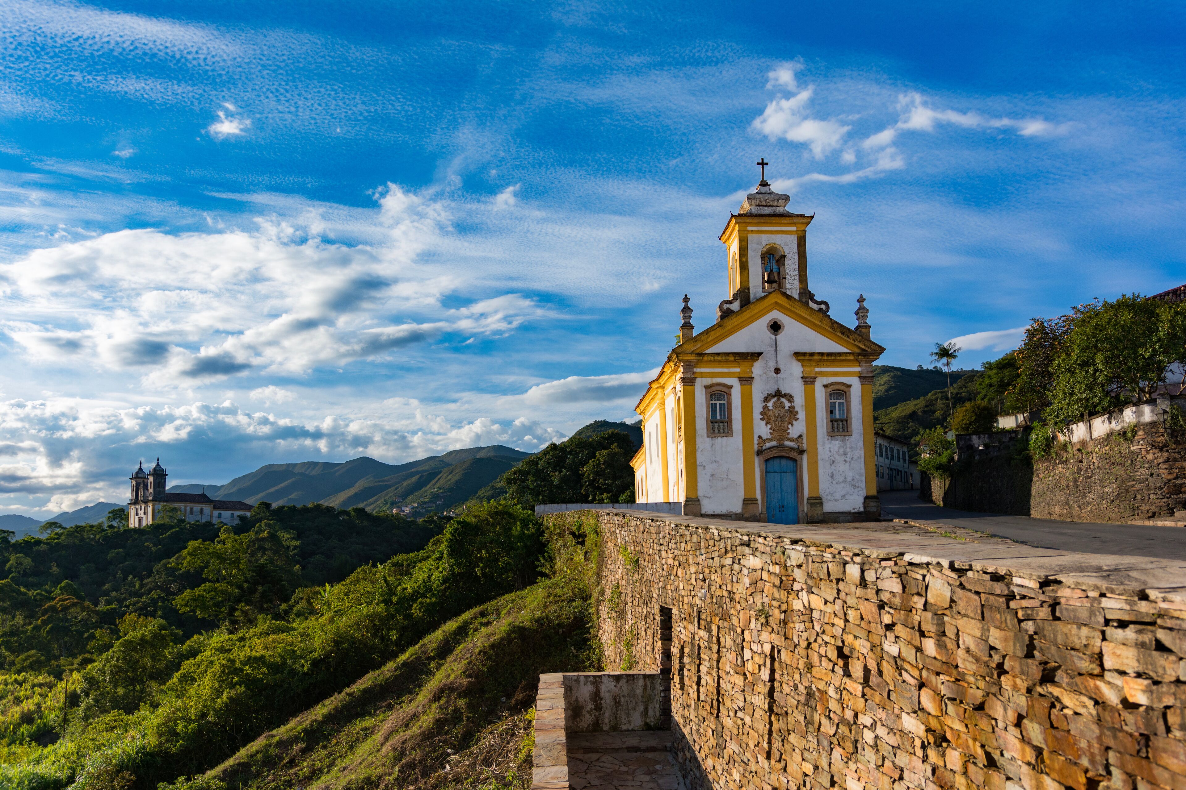 A church with a bell tower, a stone wall, and a mountain in the background.