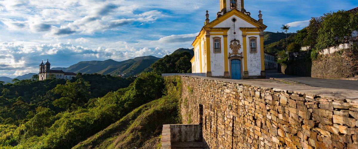 A church with a bell tower, a stone wall, and a mountain in the background.