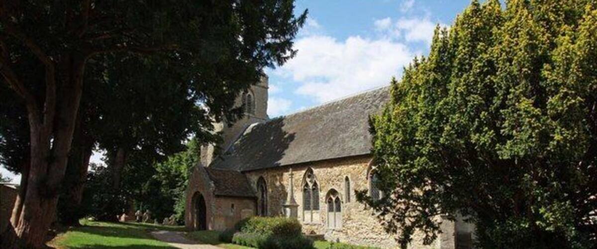 A stone church with a garden and large trees.