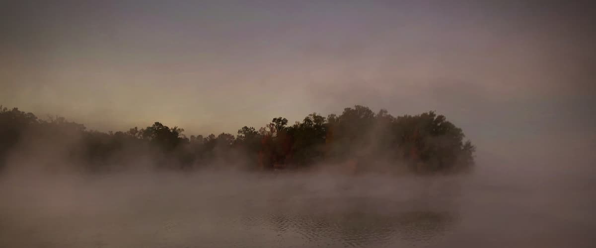 A misty lake with calm water and a forested island in the distance.