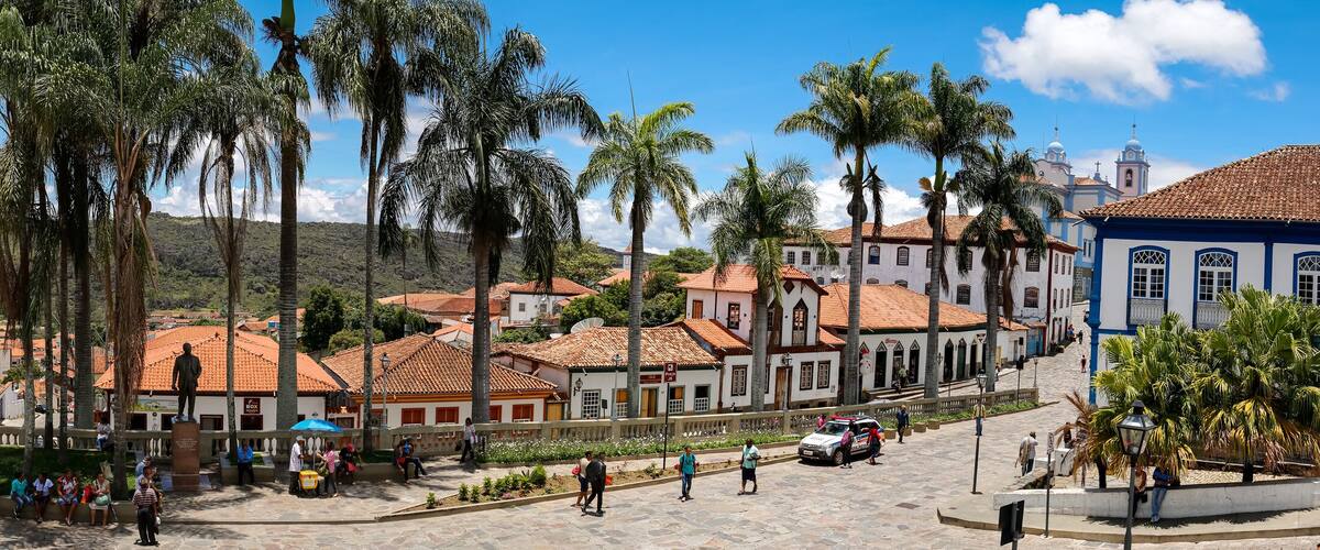 A historic town square with colonial architecture, palm trees, and a statue.