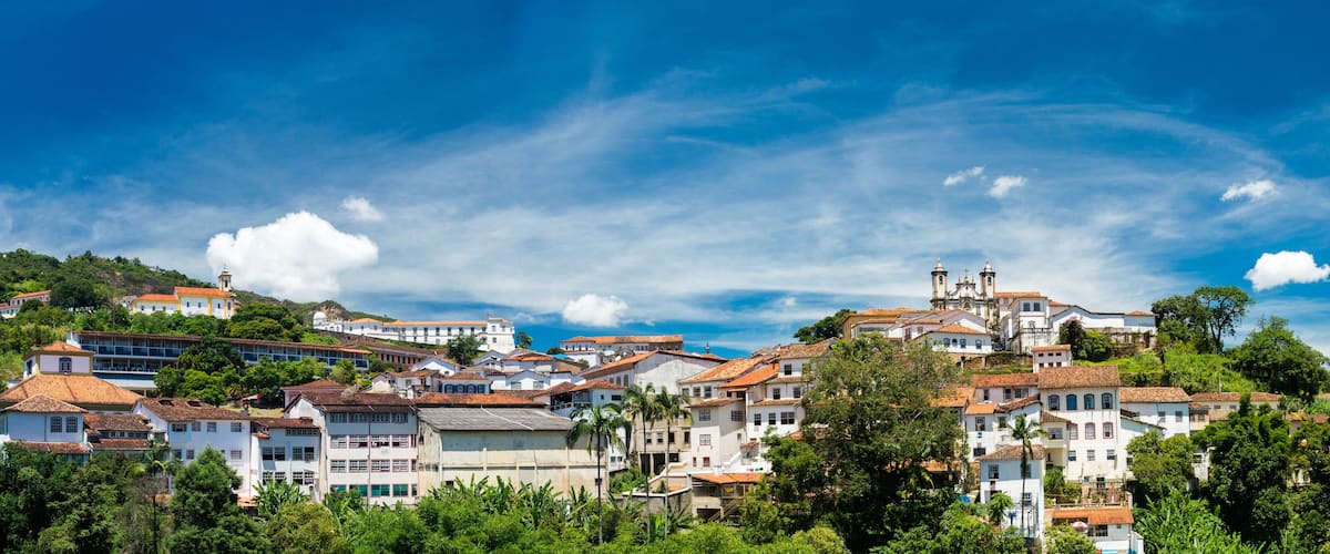 A hillside town with white buildings and red-tiled roofs, surrounded by lush greenery and a clear blue sky.