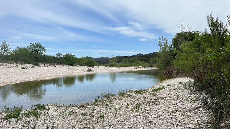 A river flowing through a rocky landscape with sparse vegetation and distant hills.