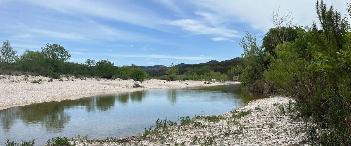A river flowing through a rocky landscape with sparse vegetation and distant hills.