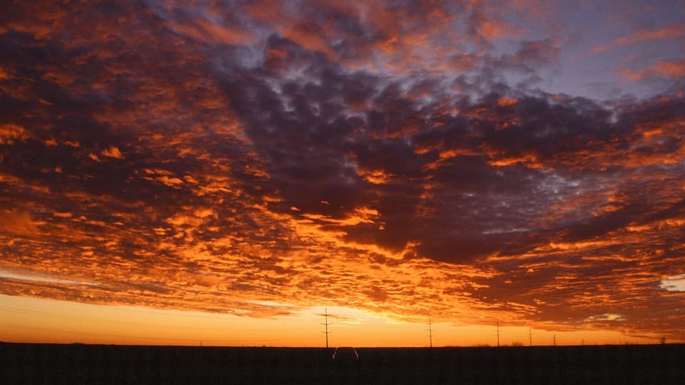 A sunset over a flat landscape with power lines and a road.
