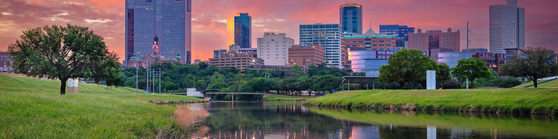 Horizonte urbano com um rio refletindo os edifícios, cercado por áreas verdes de parque.