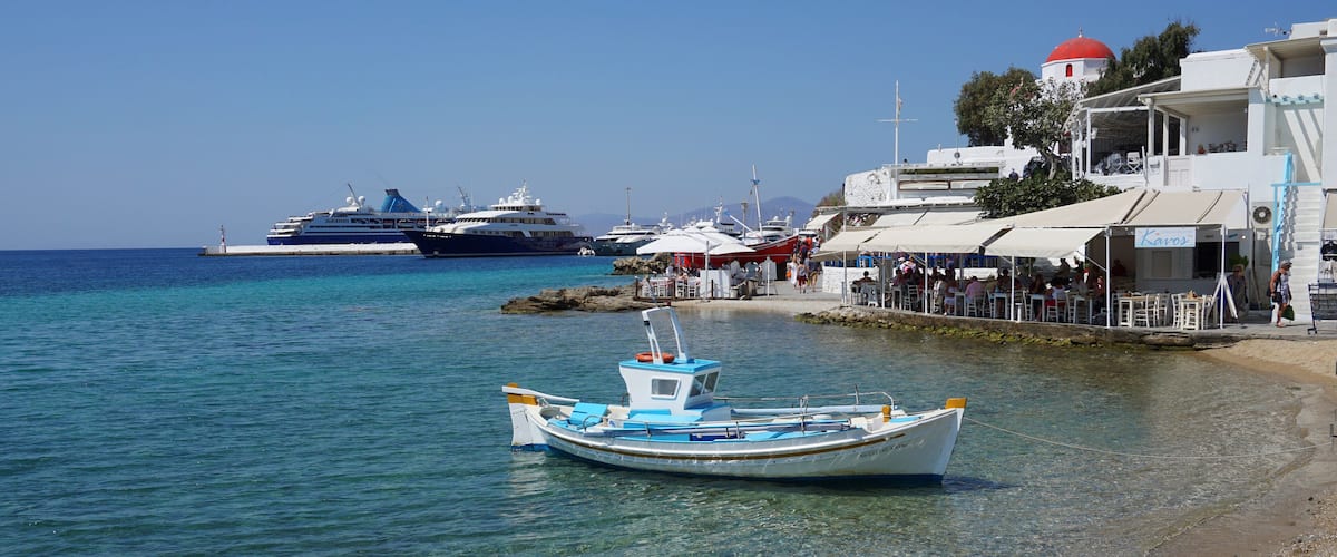 A small boat on a clear beach with larger boats in the background.