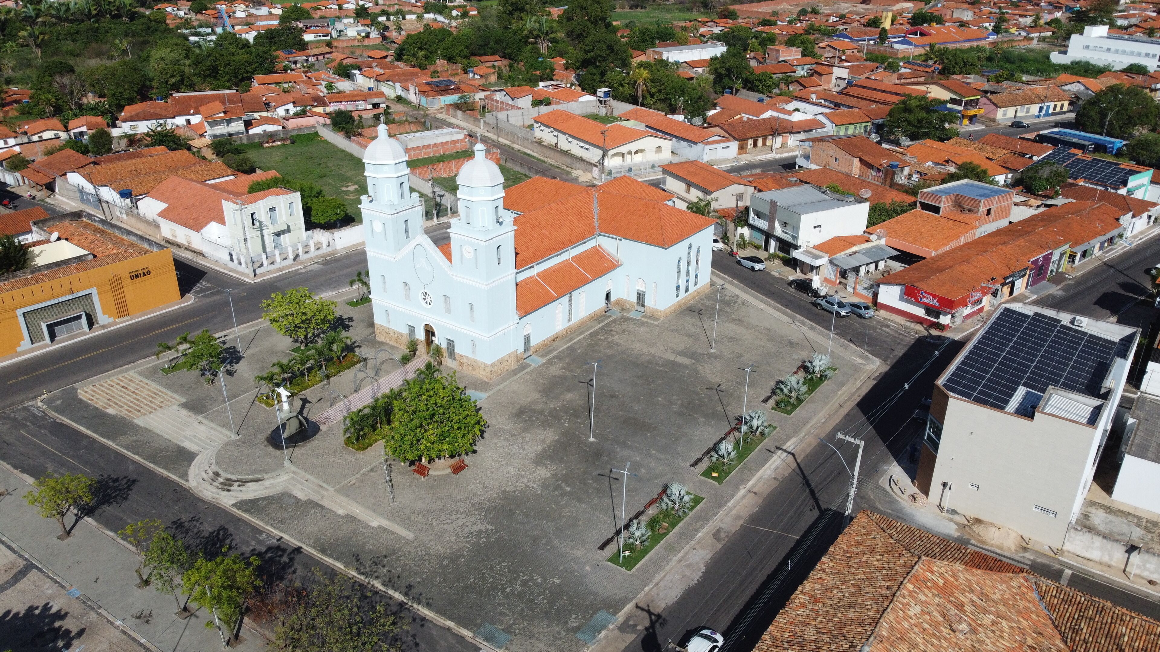 An aerial view of a town with a prominent white church with two towers, surrounded by residential buildings with red-tiled roofs.