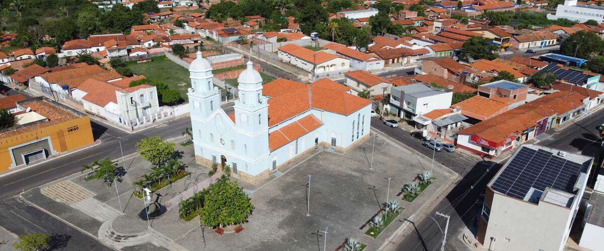 An aerial view of a town with a prominent white church with two towers, surrounded by residential buildings with red-tiled roofs.