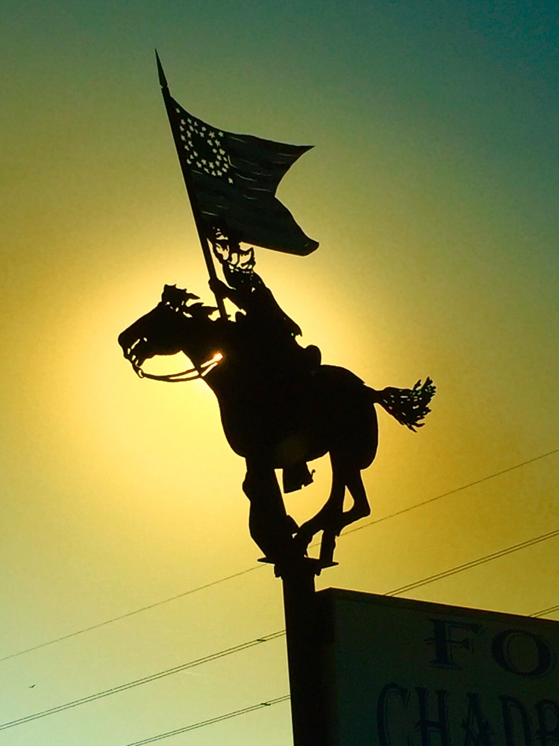 A silhouette of a horse statue with a flag, set against a sunset.