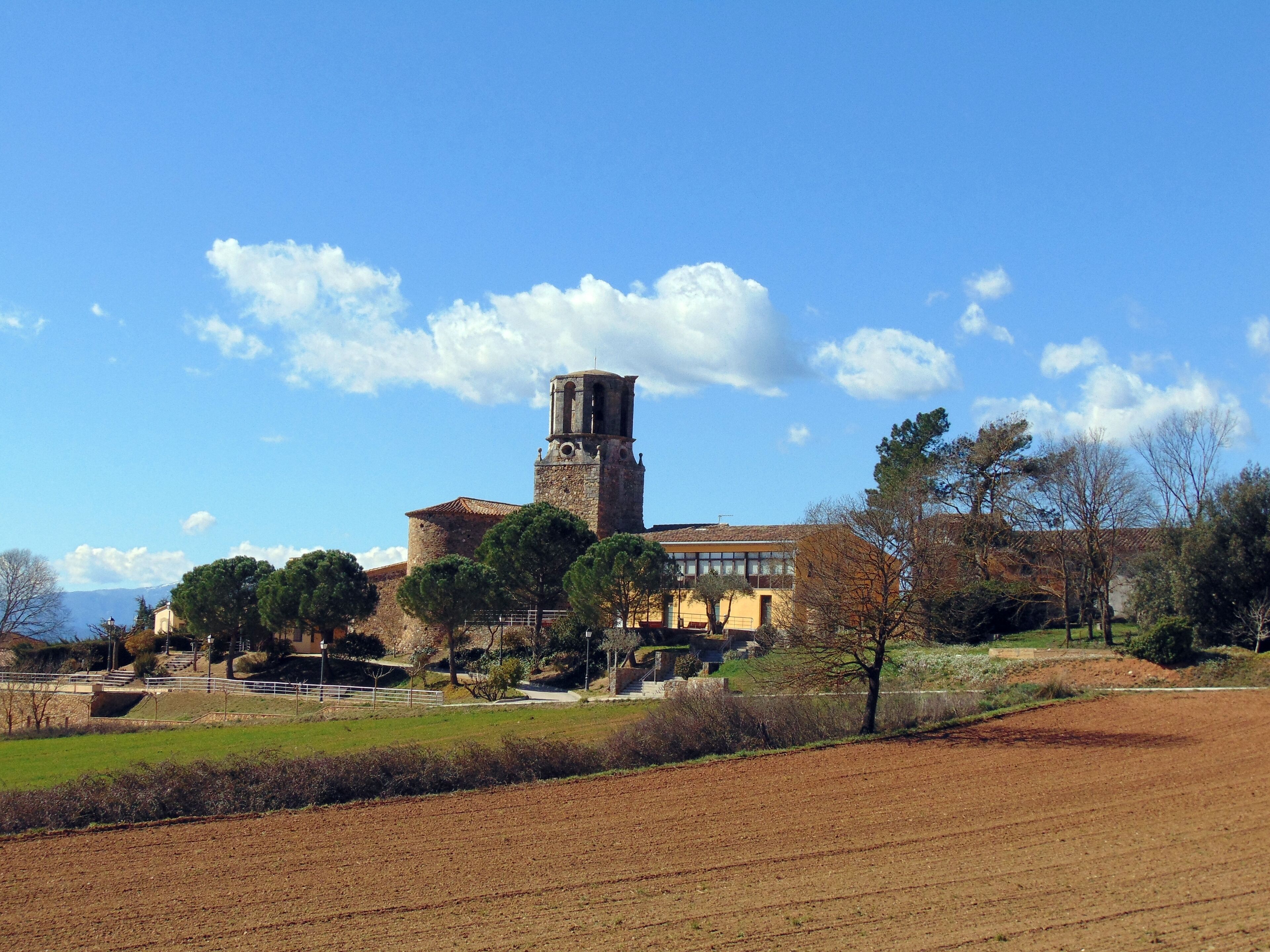A historic building with a bell tower, surrounded by trees and fields.