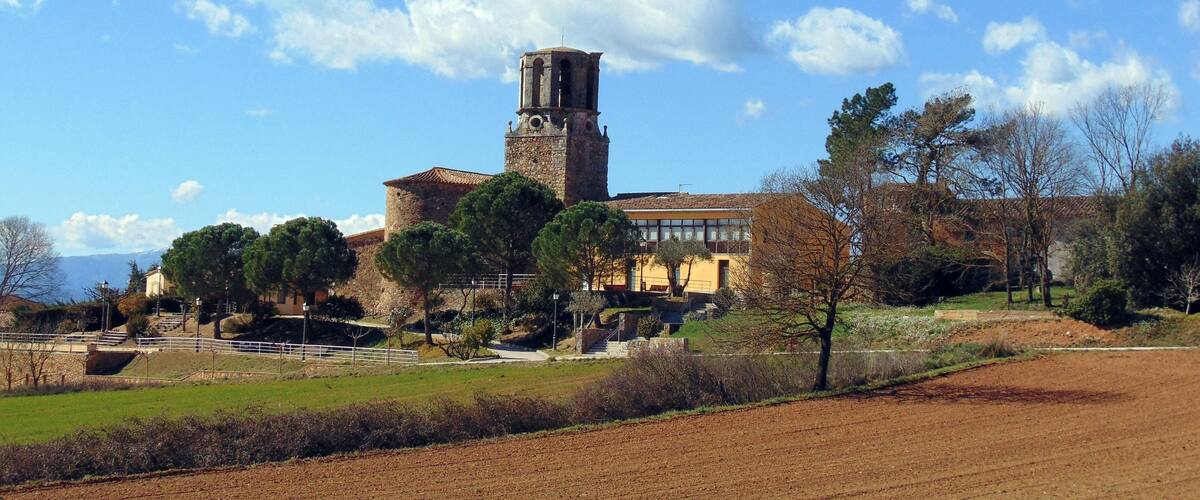 A historic building with a bell tower, surrounded by trees and fields.