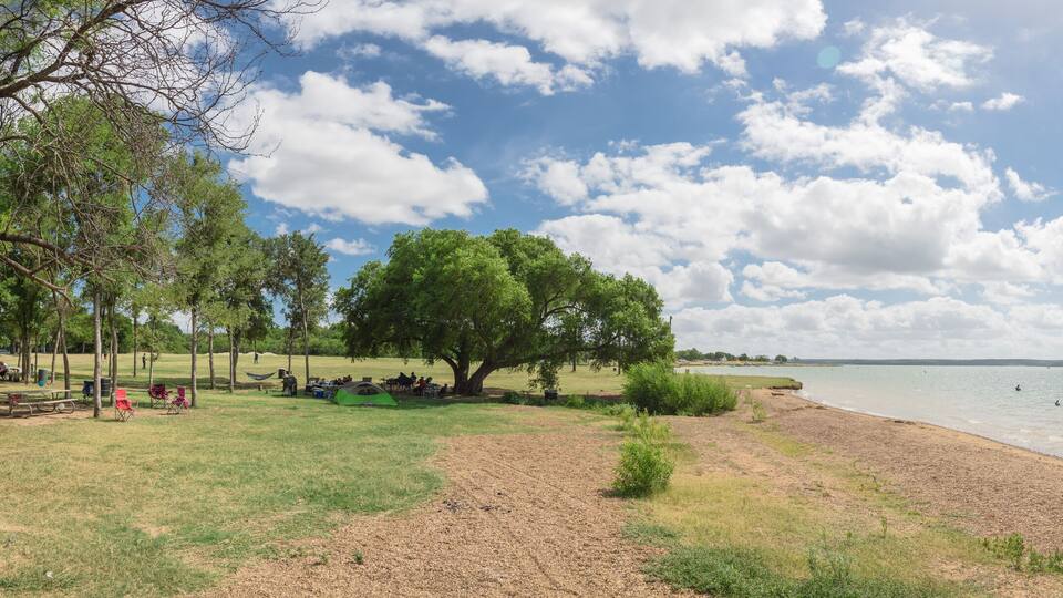 A lakeside park with picnic tables, tents, and a sandy beach.