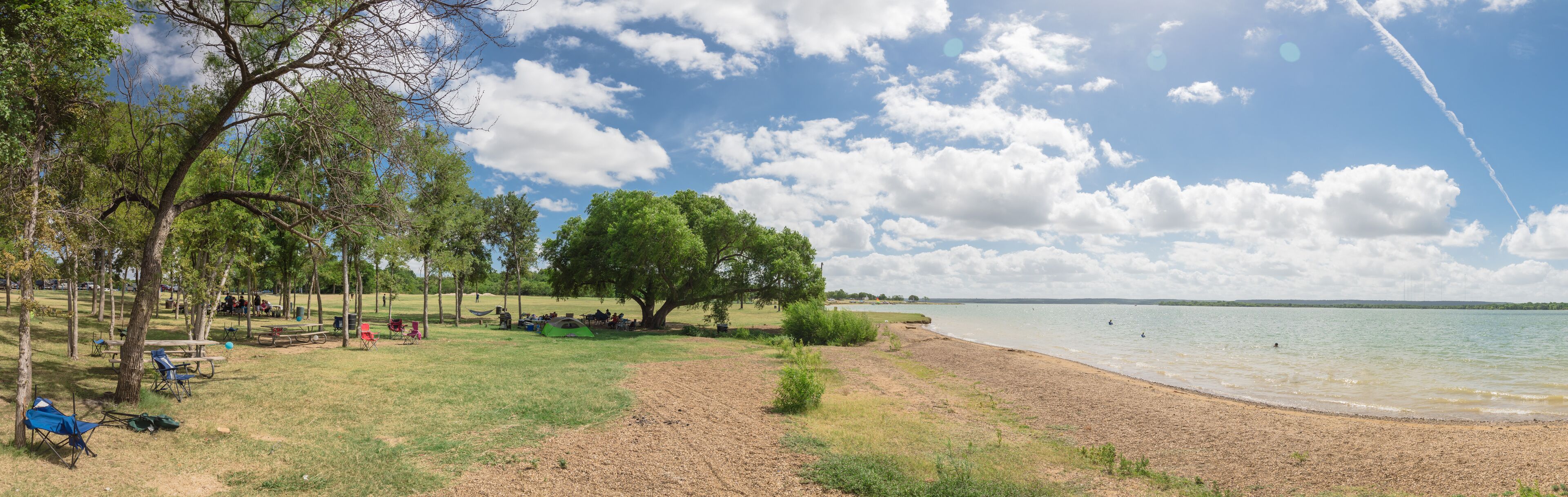 A lakeside park with picnic tables, tents, and a sandy beach.