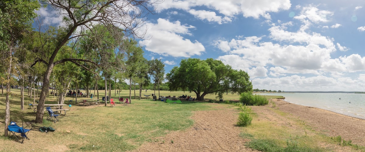 A lakeside park with picnic tables, tents, and a sandy beach.
