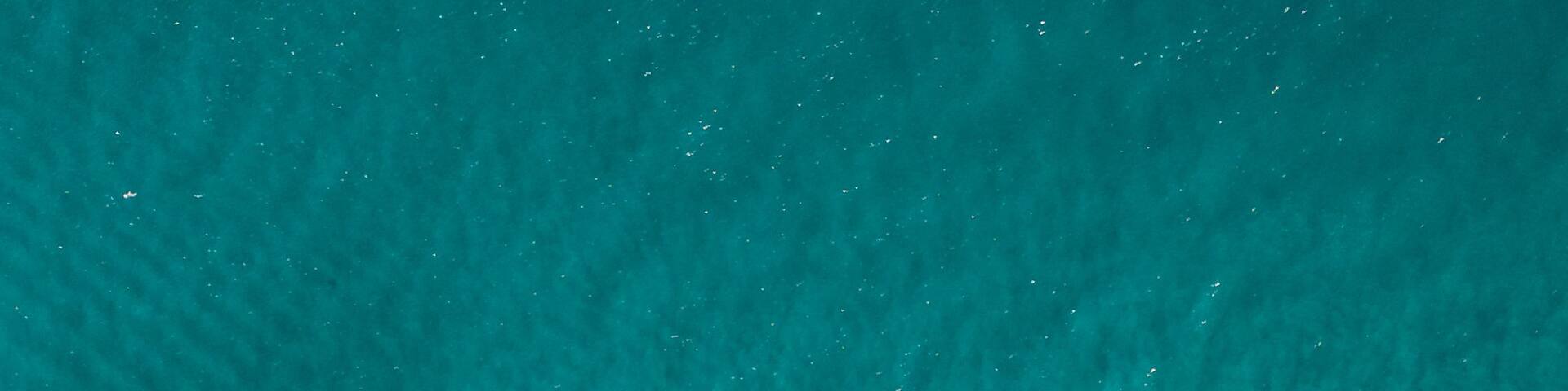An aerial view of a beach with clear turquoise water, rocky formations, and people swimming and surfing.