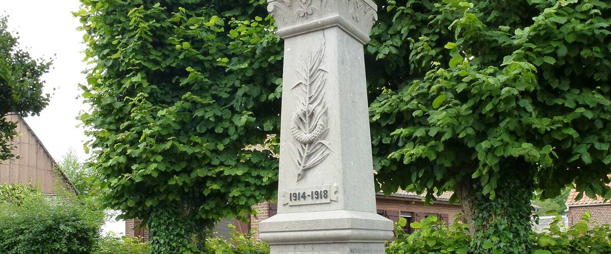 A memorial monument with inscriptions and a date range of 1914-1918, surrounded by a brick border and greenery.