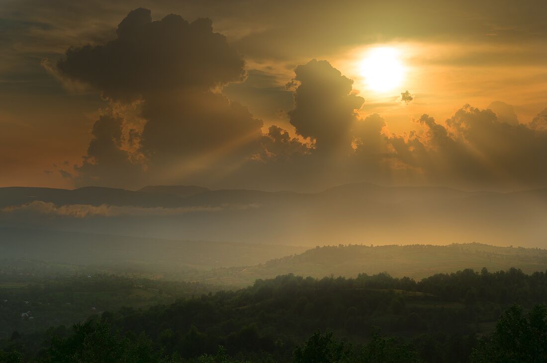 A sunrise over a hilly landscape with clouds and mist.
