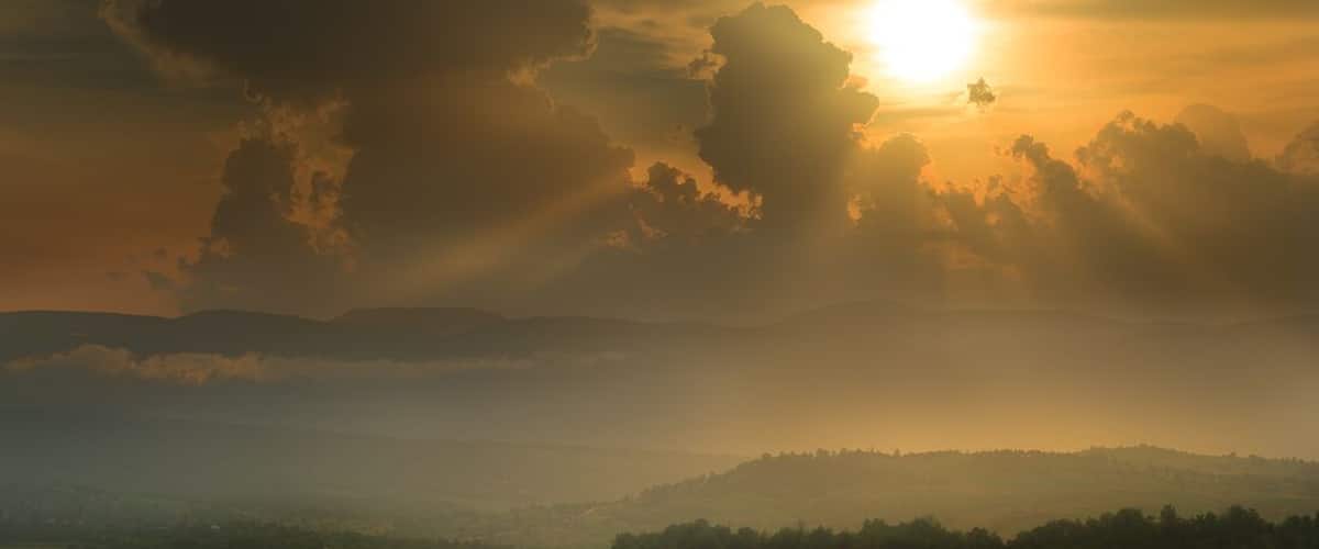A sunrise over a hilly landscape with clouds and mist.