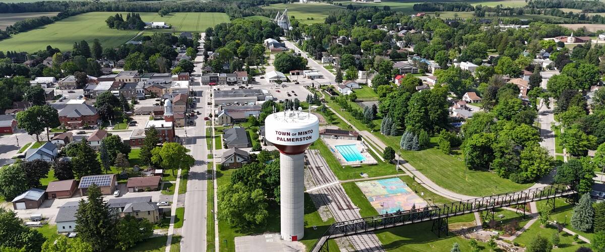 An aerial view of a town with a prominent water tower labeled 'Town of Minto Palmerston', a swimming pool, and a bridge.