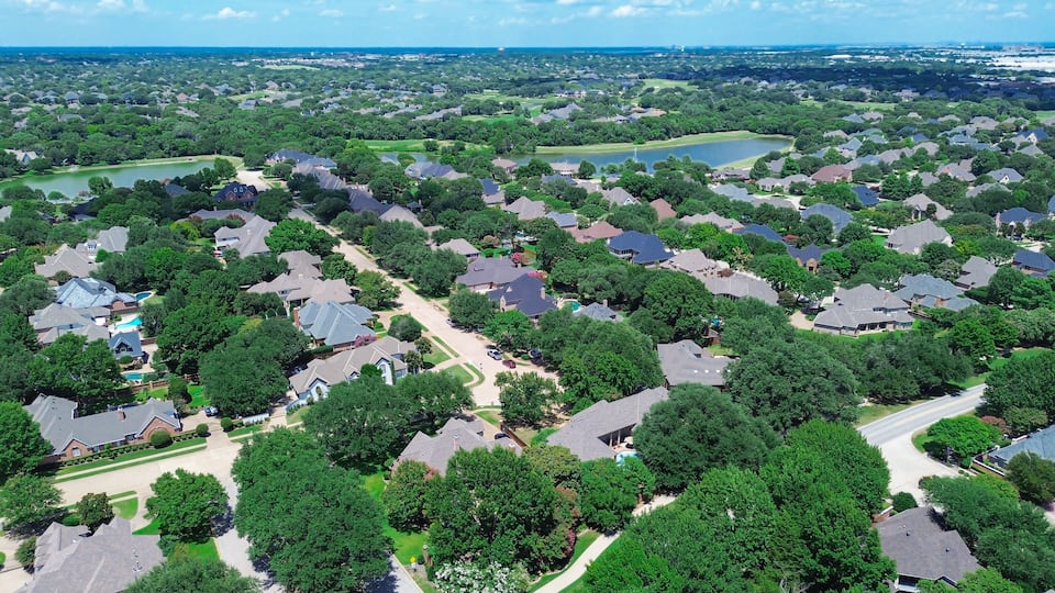 An aerial view of a residential area with houses, green lawns, and a lake.