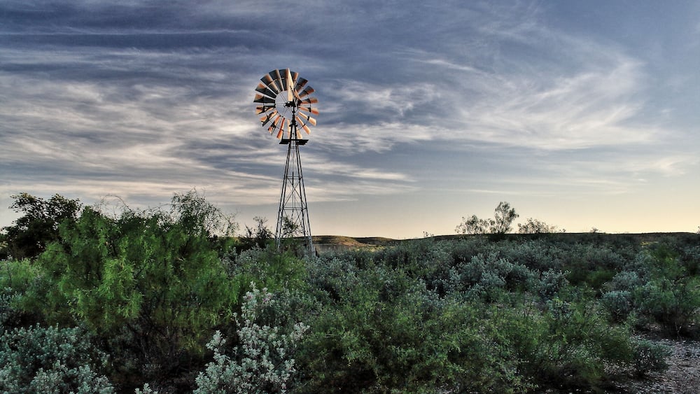 Un moulin à vent se dresse dans un champ où la végétation est clairsemée, sous un ciel nuageux.