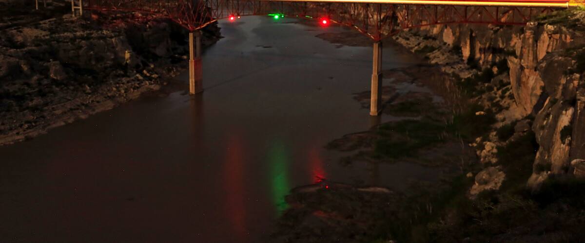 A bridge over a river at night with starry sky and reflections of lights on the water.