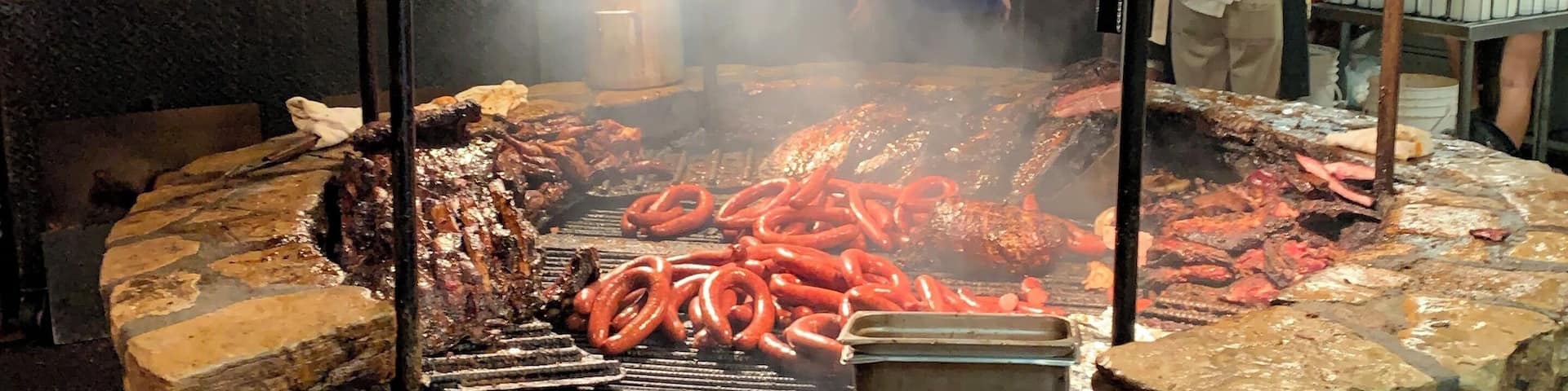 A traditional outdoor grill with sausages cooking over an open fire.