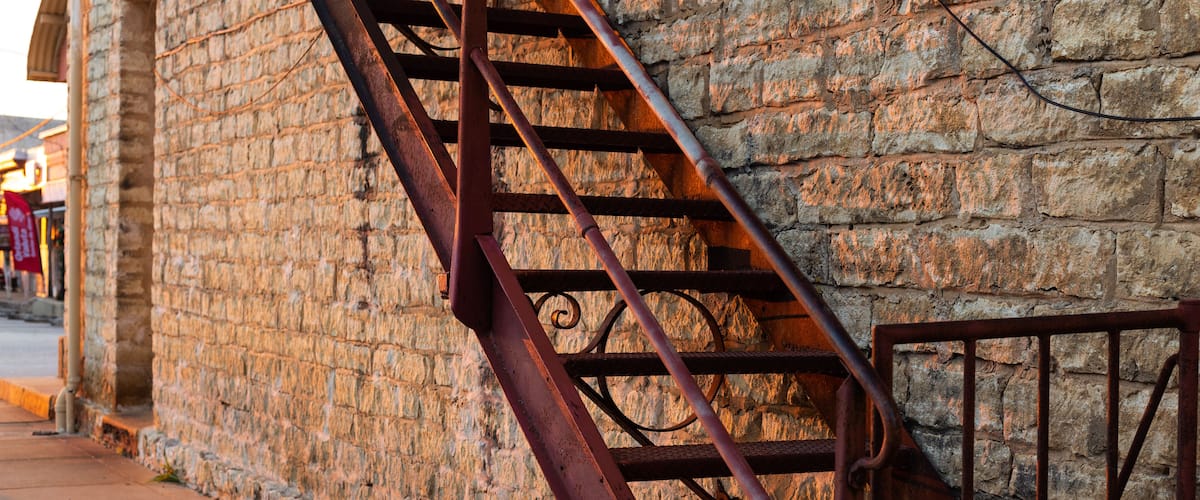Escada de incêndio de metal fixada em um edifício de pedra, com corrimão metálico e cadeado.