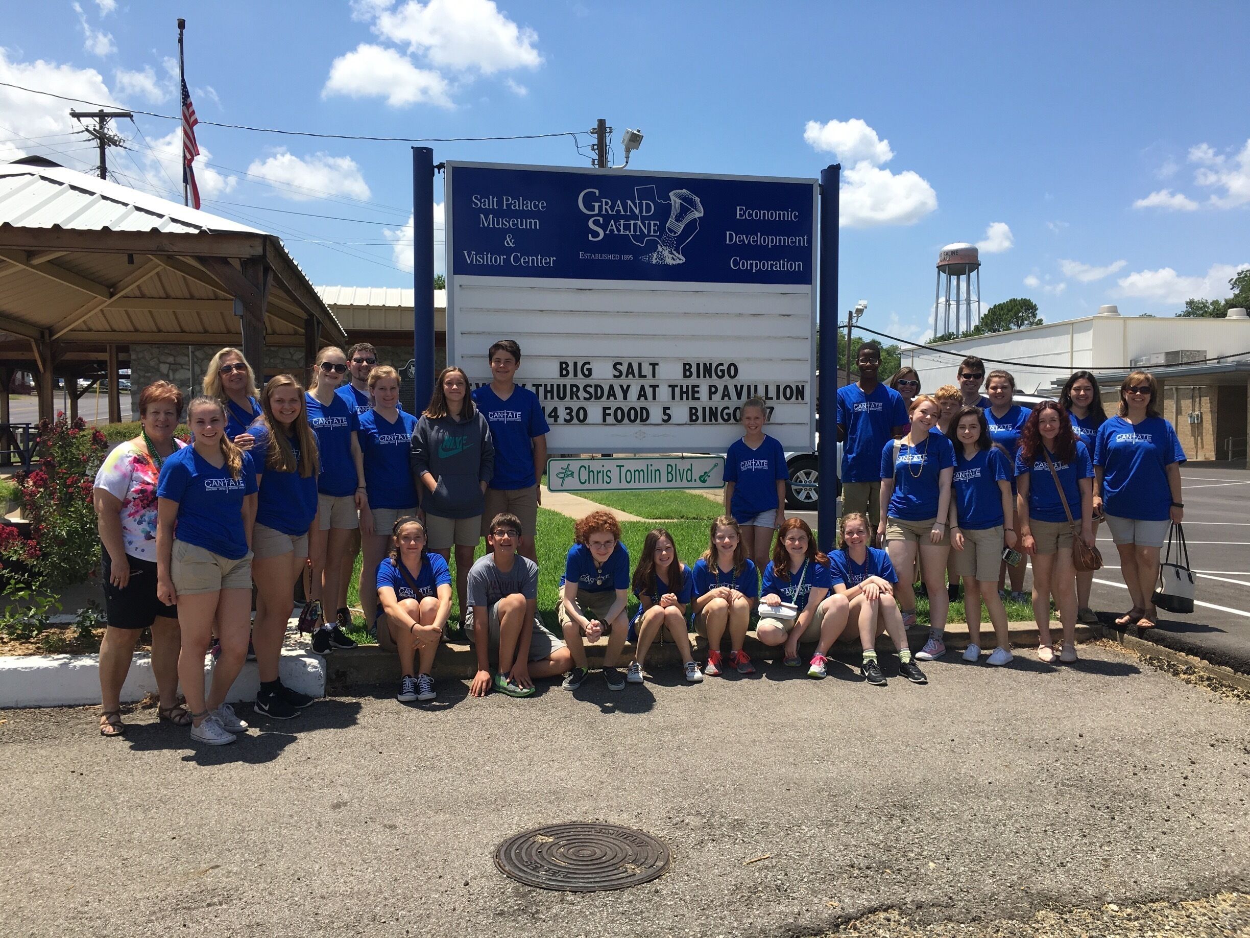 A group of people in blue shirts posing in front of a sign for the Salt Palace Museum & Visitor Center.