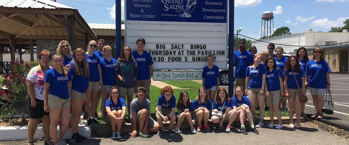 A group of people in blue shirts posing in front of a sign for the Salt Palace Museum & Visitor Center.