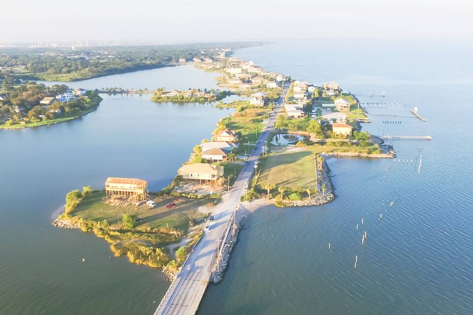 An aerial view of a coastal town with a bridge connecting to a peninsula, surrounded by water and greenery.