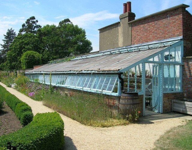 A greenhouse with a glass roof, a brick building, and a gravel path.