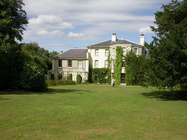 A large white house with a grey roof, surrounded by lush green trees and a well-maintained lawn.