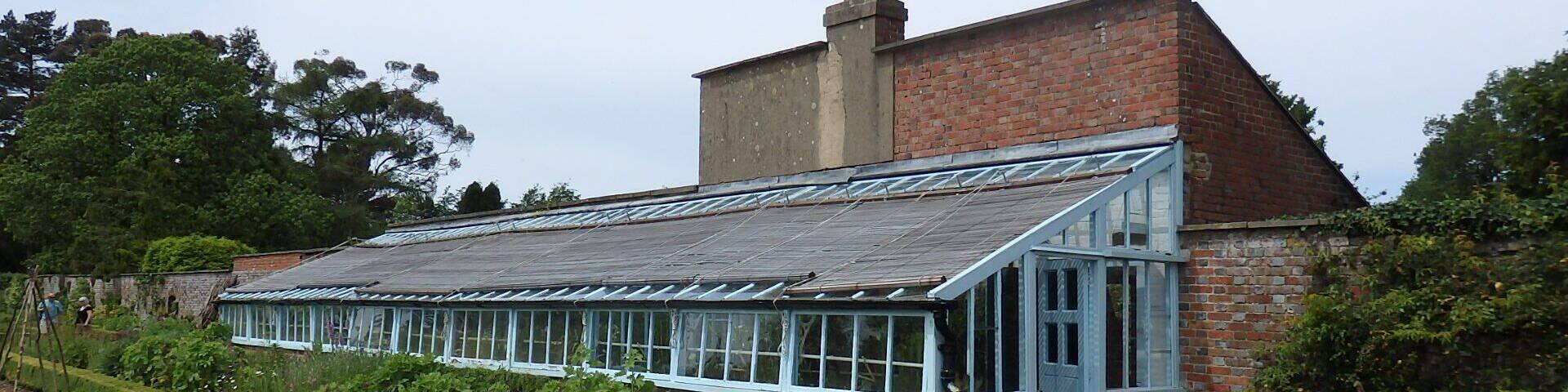 A conservatory attached to a brick house with a garden in front.