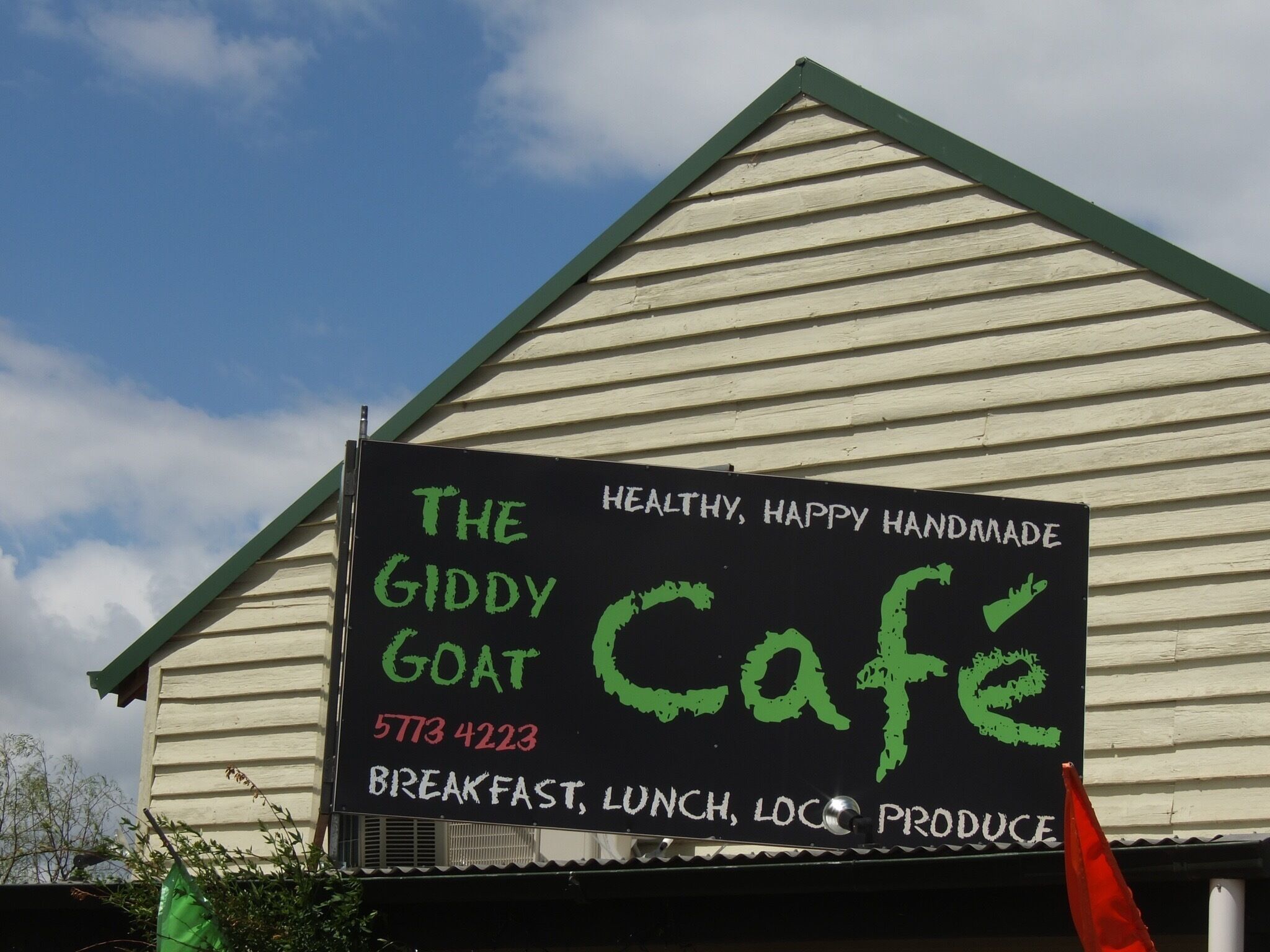 A building with a sign that reads "The Giddy Goat Cafe" offering breakfast, lunch, and local produce.
