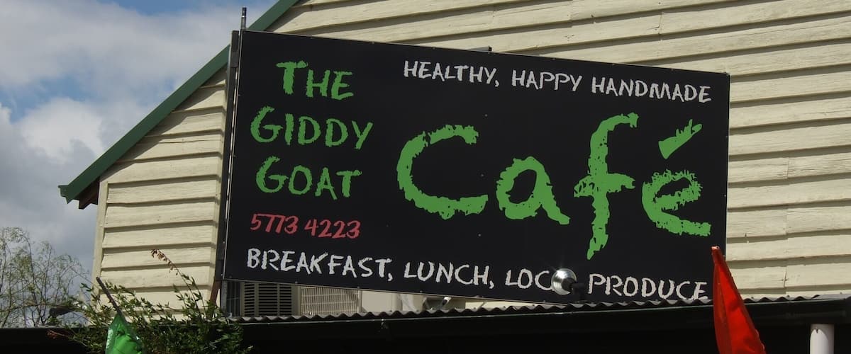 A building with a sign that reads "The Giddy Goat Cafe" offering breakfast, lunch, and local produce.