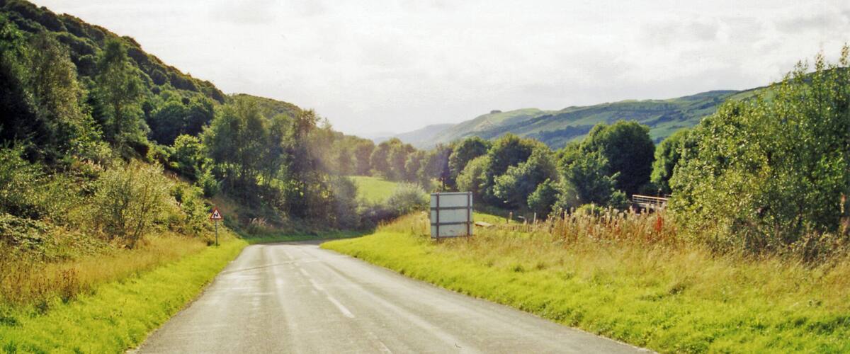 A rural road flanked by lush greenery and hills.
