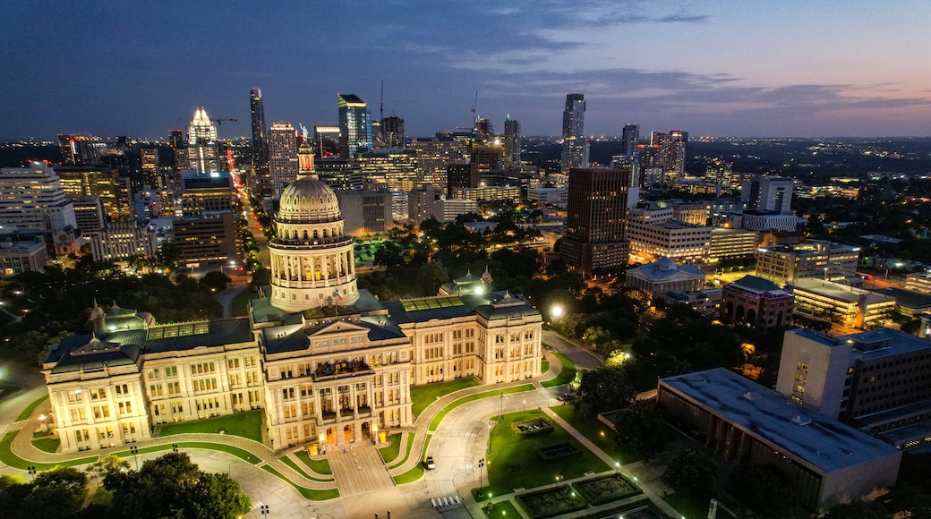 A cityscape at dusk with a prominent historic building with a dome in the center, surrounded by modern skyscrapers and well-lit streets.
